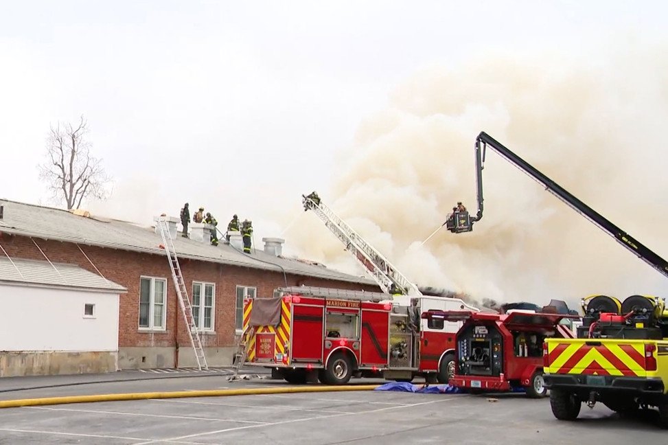 Aerial ladder operations and rooftop firefighting efforts to control fire spread across interconnected campus buildings.