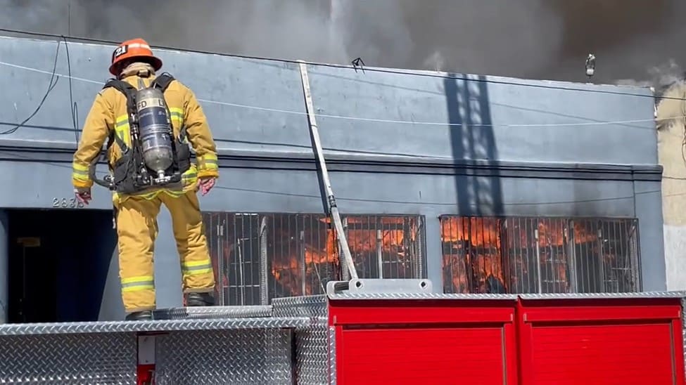 A firefighter assesses ongoing fire inside warehouse. 